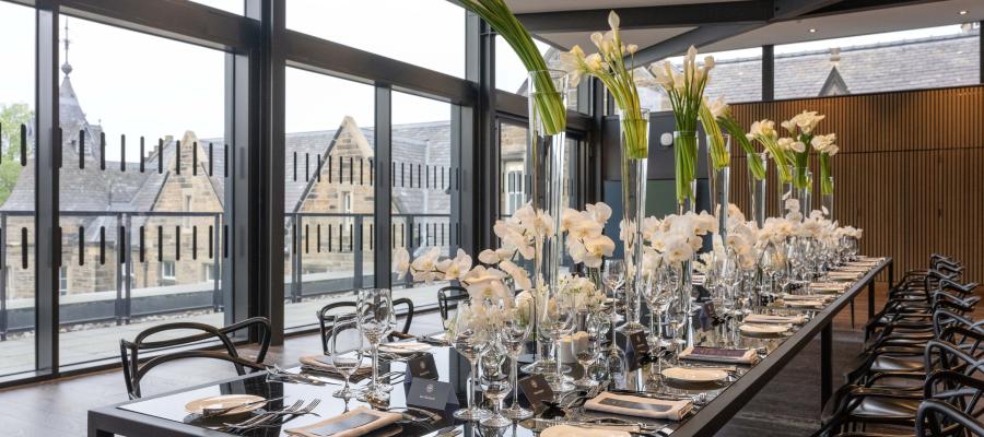 An elaborate table setting with tall flower arrangements for an exclusive black-tie dinner in room 4.55 at the Edinburgh Futures Institute at 1 Lauriston Place, Edinburgh